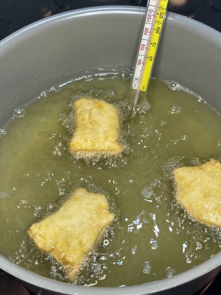 beignets frying in a pot of oil on a stove with a thermometer